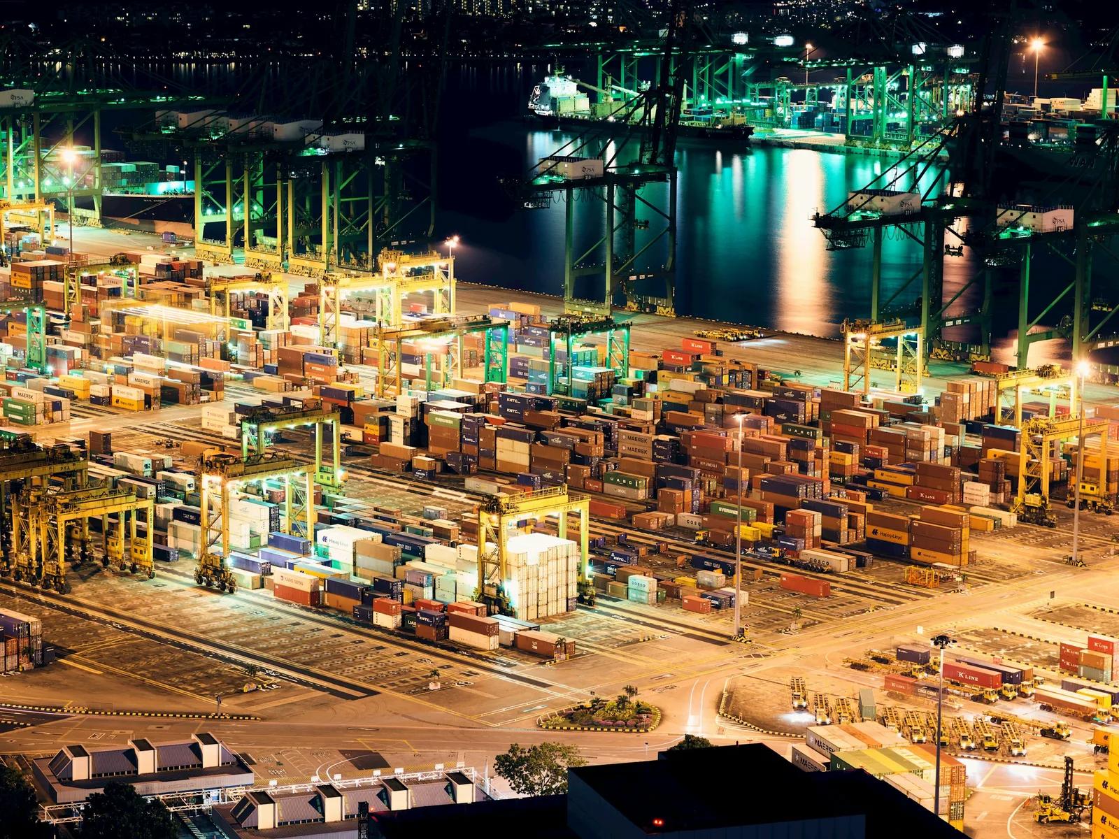 Container terminal operating at night with cranes, cargo stacks, and illuminated docks